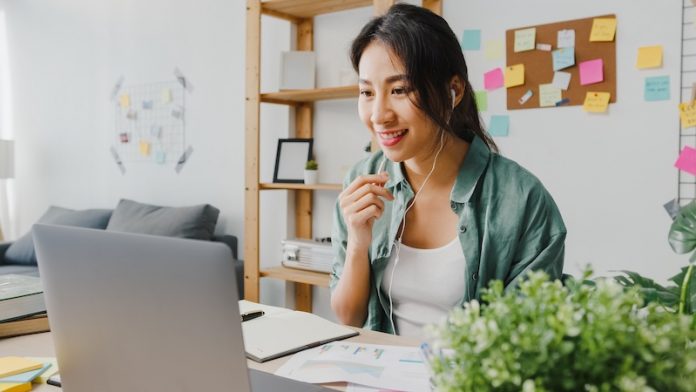 Asia businesswoman using laptop talk to colleagues about plan in video call while smart working from home at living room. Self-isolation, social distancing, quarantine for corona virus prevention.